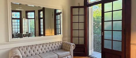Una habitación amplia con un espejo grande, un sofá capitonado, una mesa de centro y un ventanal con vitrales.