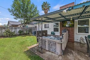 A backyard with a hot tub, a covered patio, and a wooden fence. - Your Riverside Retreat. (Riverside)