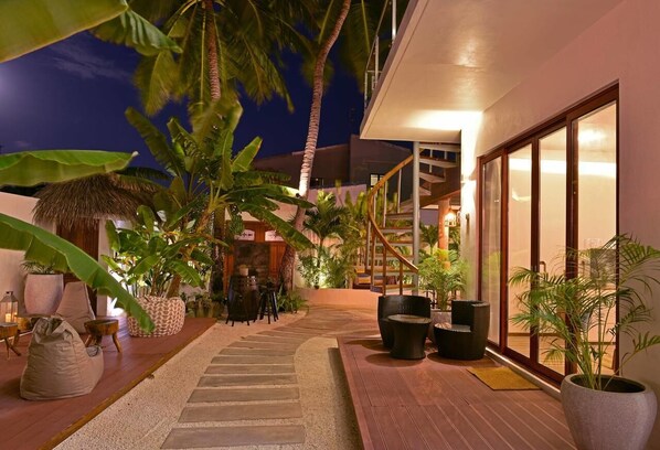A well-lit outdoor area with a wooden deck, potted plants, and a staircase leading to a building.