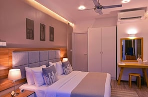 A modern hotel room with a large bed, bedside table, lamp, and a desk with a mirror.