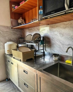 A compact kitchen with a sink, a dish rack, a microwave, and a water bottle on the countertop.