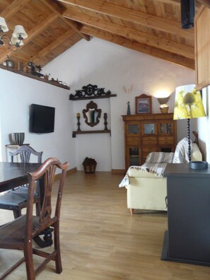 A dining area with a wooden table and chairs, a television on the wall, and a cabinet with a mirror and decorative items. - A House with Beautiful Sunrises (El rosario)