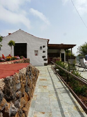 A pathway leading to a building with a stone wall on one side and a patio area with outdoor furniture. - A House with Beautiful Sunrises (El rosario)