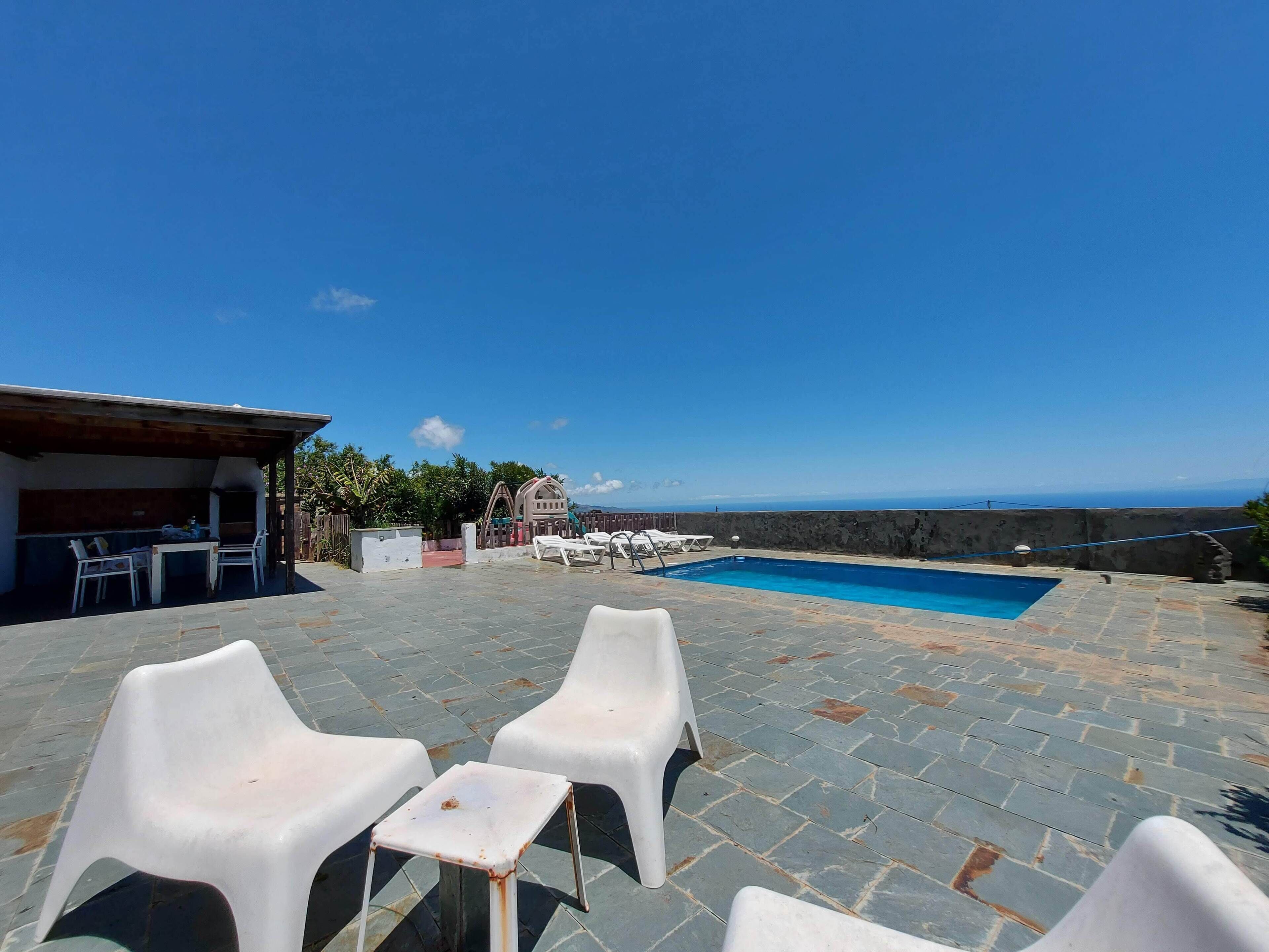Un espace extérieur avec piscine, des chaises longues, un barbecue et une vue sur la mer.