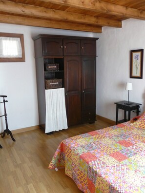 A bedroom with a wooden ceiling, a bed with a colorful quilt, a dark wooden wardrobe, a small table with a lamp, and a window with a curtain. - A House with Beautiful Sunrises (El rosario)
