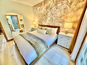 A bedroom with a large bed, two bedside tables, a nightstand, a mirror, and a wall with a tree mural. - 1020/22 | Stylish 2BR Villa | Sleeps 8 | Near Park City Skiing (Midway)