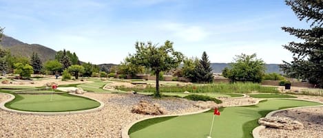 Un campo de mini golf con varios hoyos, rodeado de árboles y un paisaje montañoso al fondo.