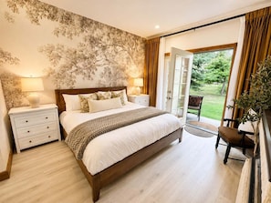 A bedroom with a large bed, a nightstand, a chair, and a view of the outdoors through a glass door. - 1022 | Remodeled King Villa | Full Kitchen | Pool (Midway)