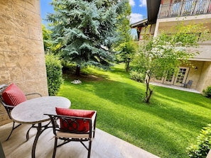A patio with a round table and two chairs, a small tree, and a well-maintained lawn. - 1022 | Remodeled King Villa | Full Kitchen | Pool (Midway)
