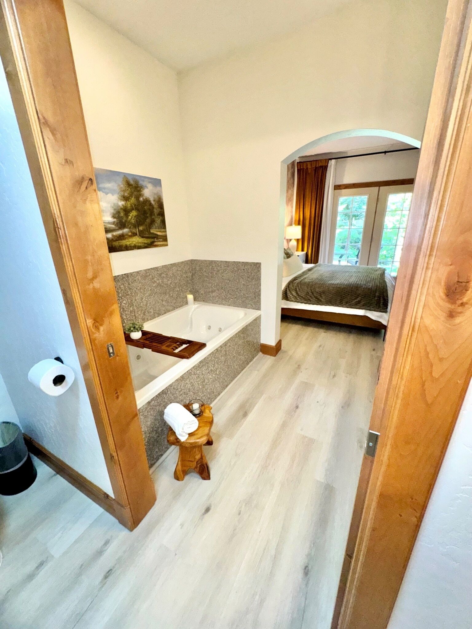 A bedroom with a bed, a bathroom with a bathtub, and a small wooden stool.