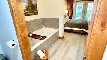 A bedroom with a bed, a bathroom with a bathtub, and a small wooden stool.