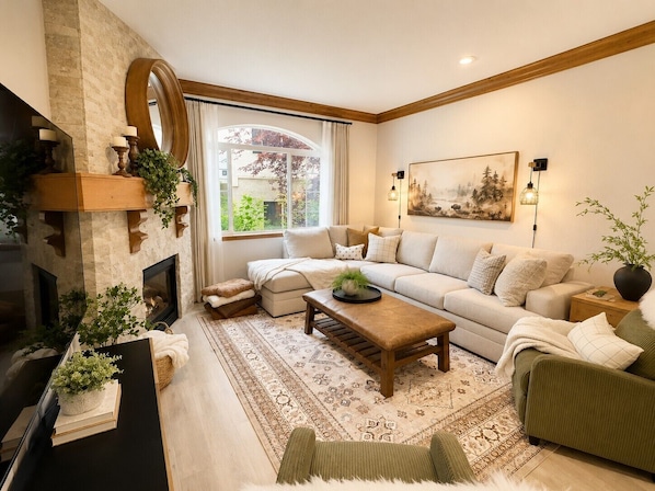 A cozy living room with a fireplace, a sofa set, a coffee table, and a large window with curtains. - 1022 | Remodeled King Villa | Full Kitchen | Pool (Midway)