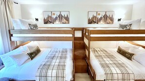 A room with two bunk beds, each with a pillow and a blanket. There are two wall-mounted picture frames with mountain scenes.