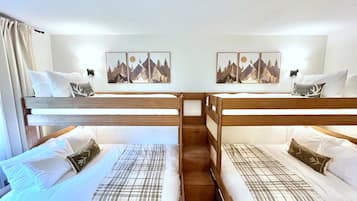 A room with two bunk beds, each with a pillow and a blanket. There are two wall-mounted picture frames with mountain scenes.