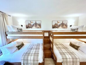Ein Zimmer mit zwei Etagenbetten, jeweils mit Kissen und Decke. An der Wand hängen zwei Bilder von Berglandschaften.