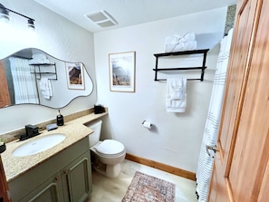Un bagno con doppio lavabo, un water, un appendi asciugamani e un quadro incorniciato al muro.