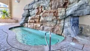 A swimming pool with a rocky wall backdrop, a metal ladder, and a tiled floor.