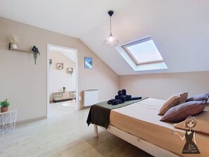 Een slaapkamer met dakraam, een bed met kussens, een nachtkastje en een hangplant.