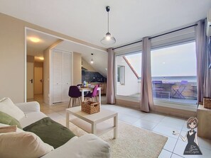 A modern living room with a sofa, a coffee table, and a view of the sea through large windows.