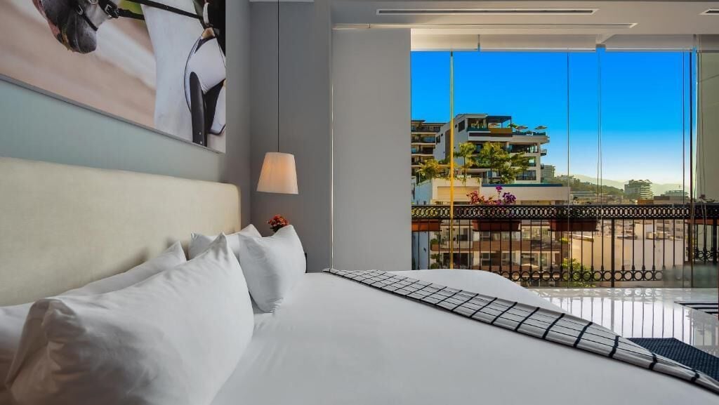 Ein Hotelzimmer mit einem großen Bett, einem Balkonblick auf Gebäude und eine Stadtansicht.