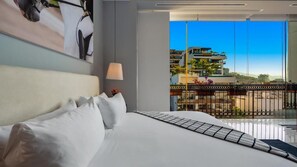 Ein Hotelzimmer mit einem großen Bett, einem Balkonblick auf Gebäude und eine Stadtansicht.