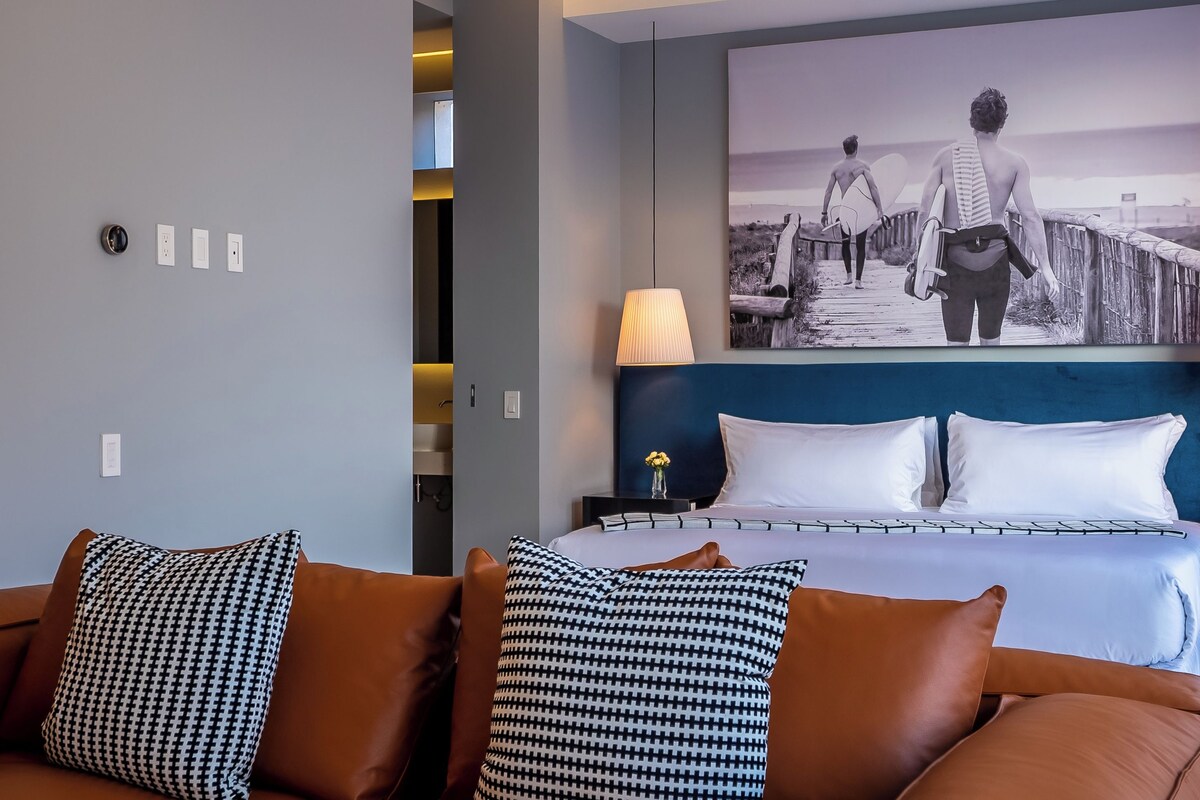 Ein Hotelzimmer mit einem Bett, einem Kopfteil, einem Nachttisch, einer Lampe und einem Wandbild.