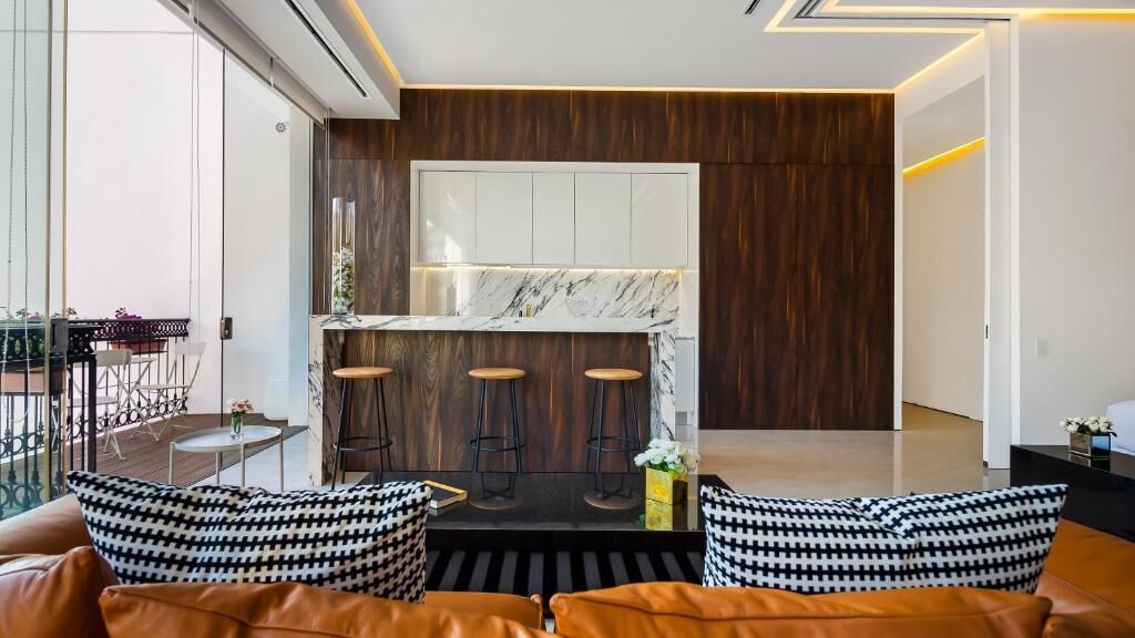 Una cocina moderna con encimera de mármol, armarios de madera y una zona de bar con taburetes.