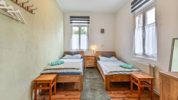 Un dormitorio con dos camas, suelo de madera, ventana y radiador.