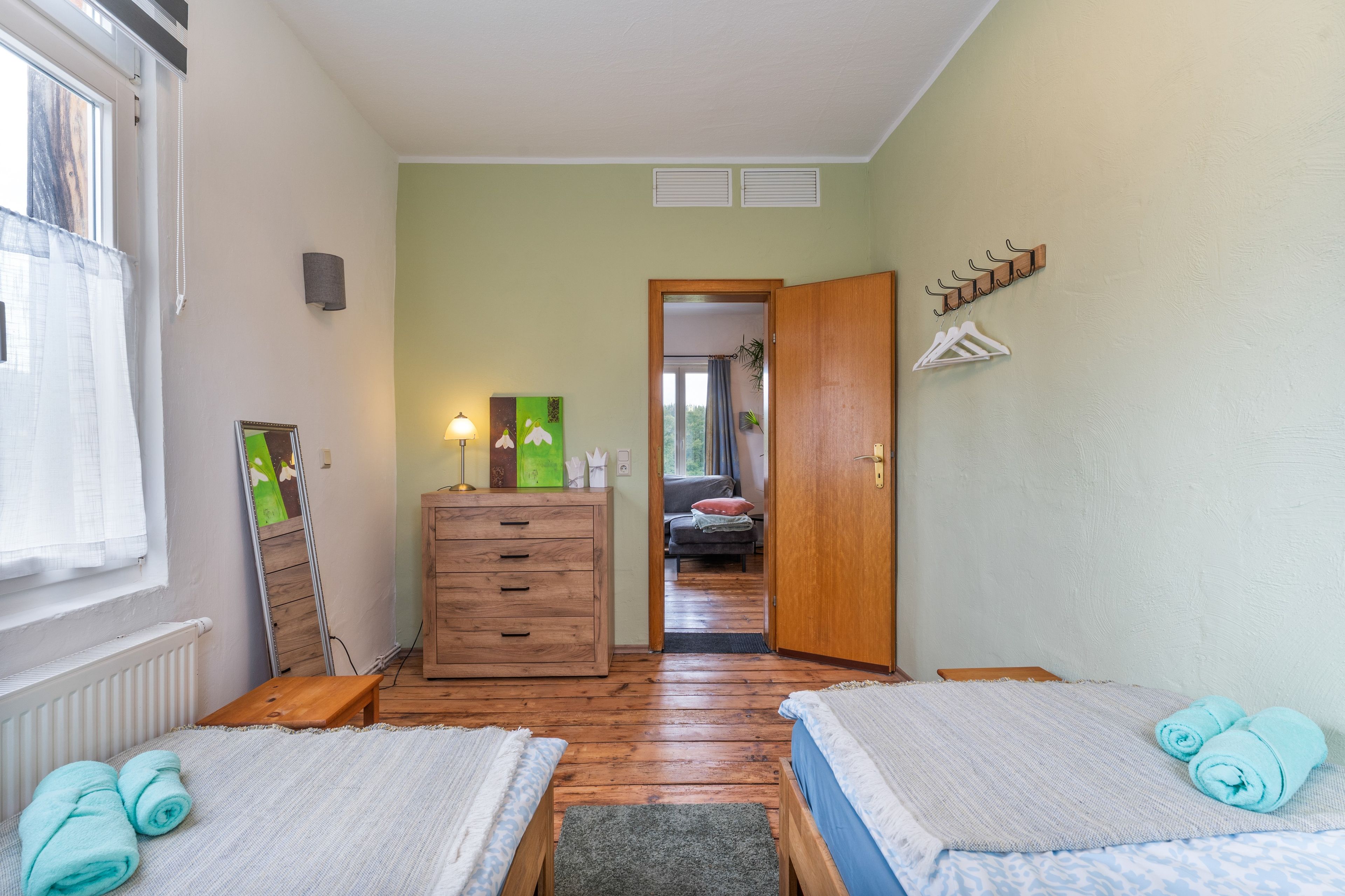 A room with two beds, a wooden dresser, a lamp, and a view of a balcony.