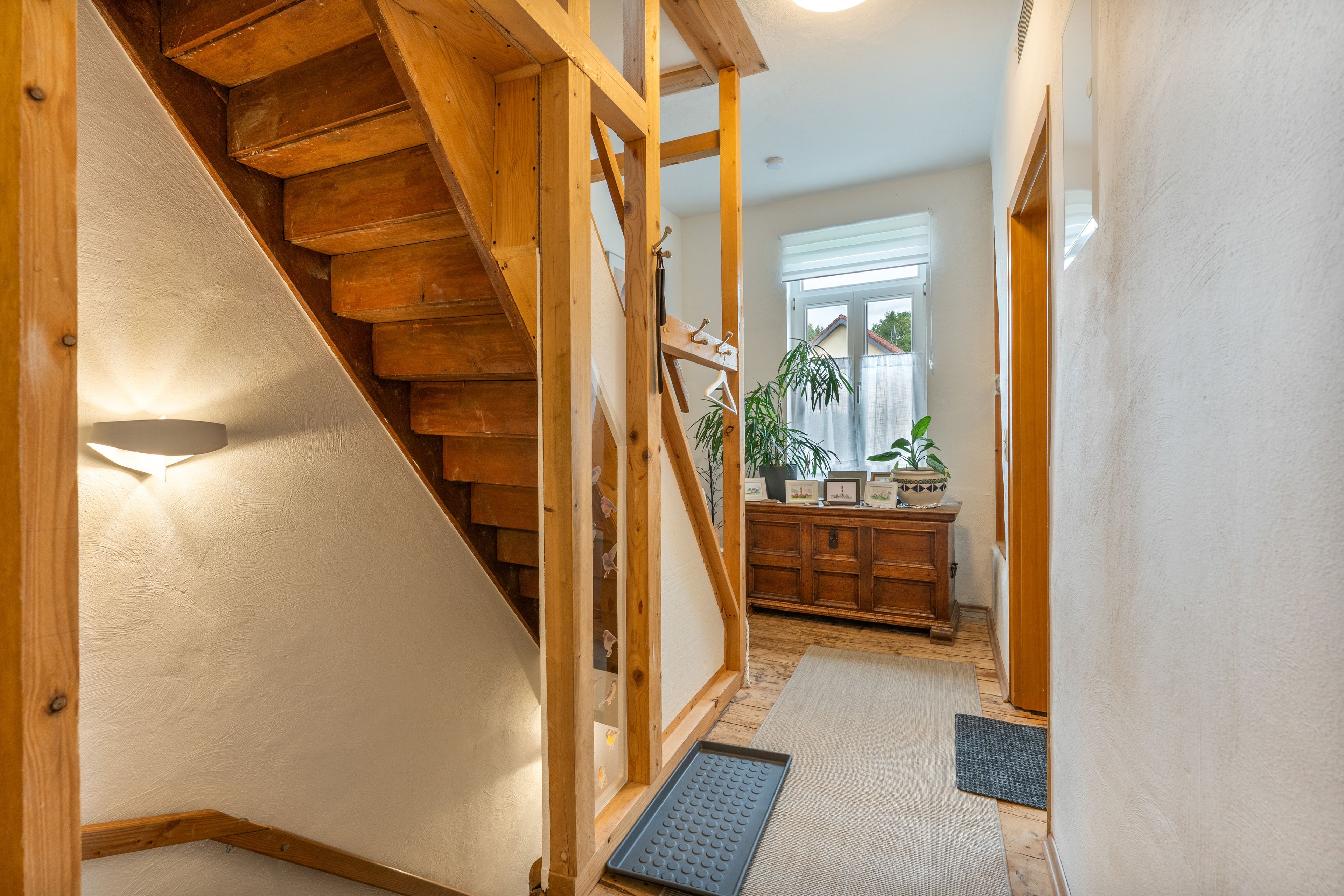 A wooden staircase leading to a landing with a view of a window and a plant.