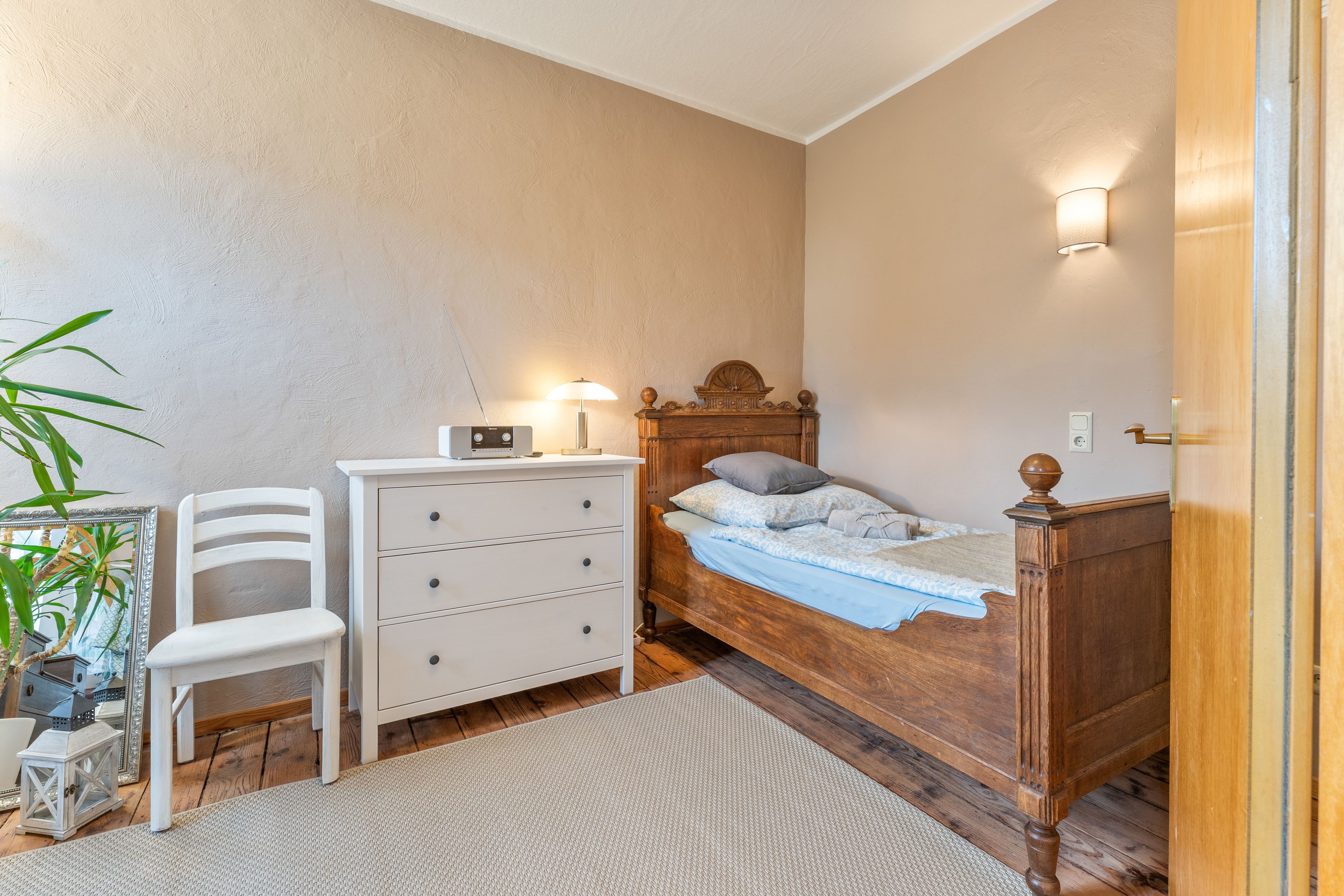 Ein Schlafzimmer mit einem hölzernen Bett, einer weißen Kommode, einem Sessel und einem Nachttisch mit einer Lampe.