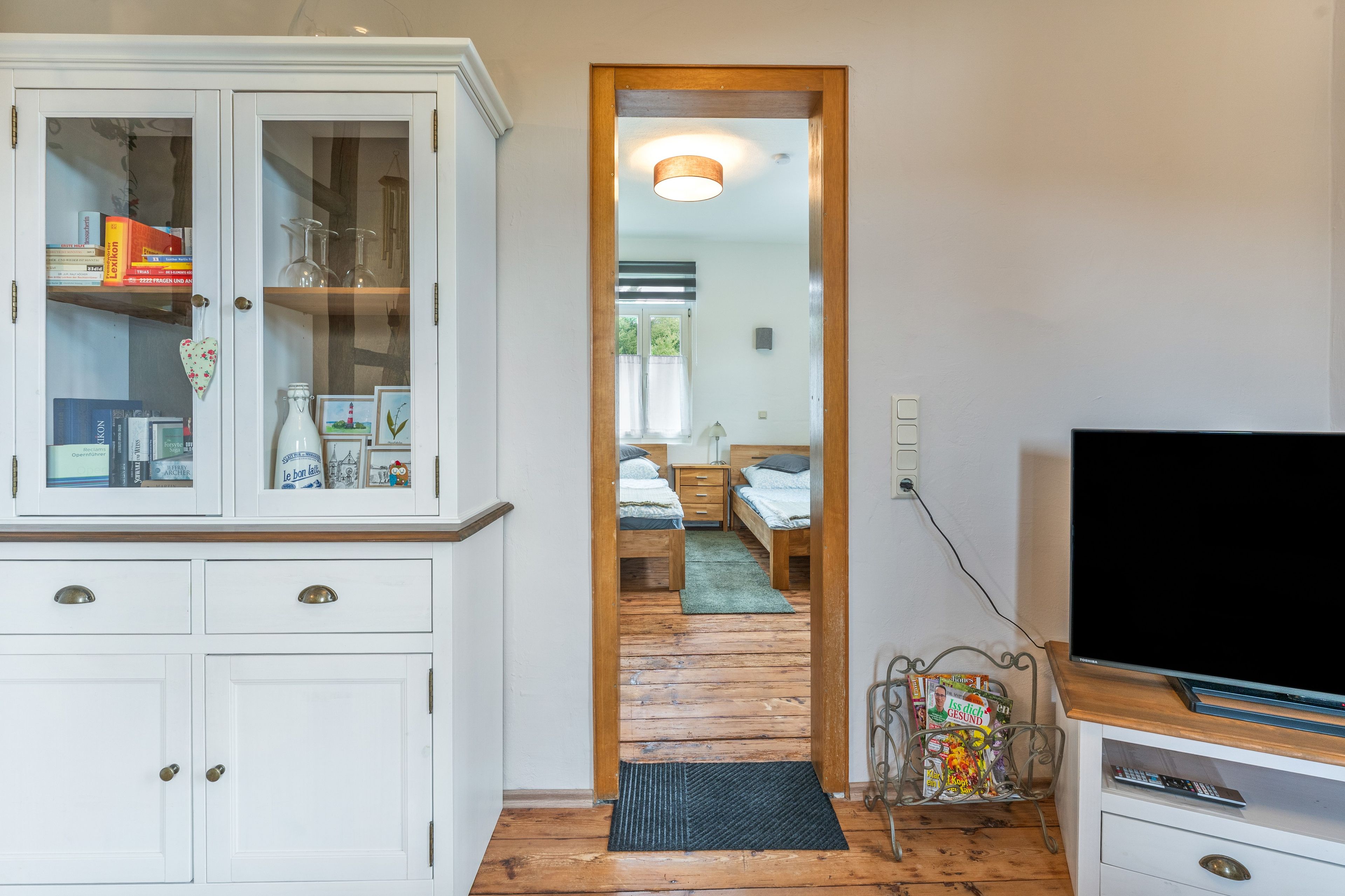 Una habitación con un armario blanco, televisor y cama sobre piso de madera.