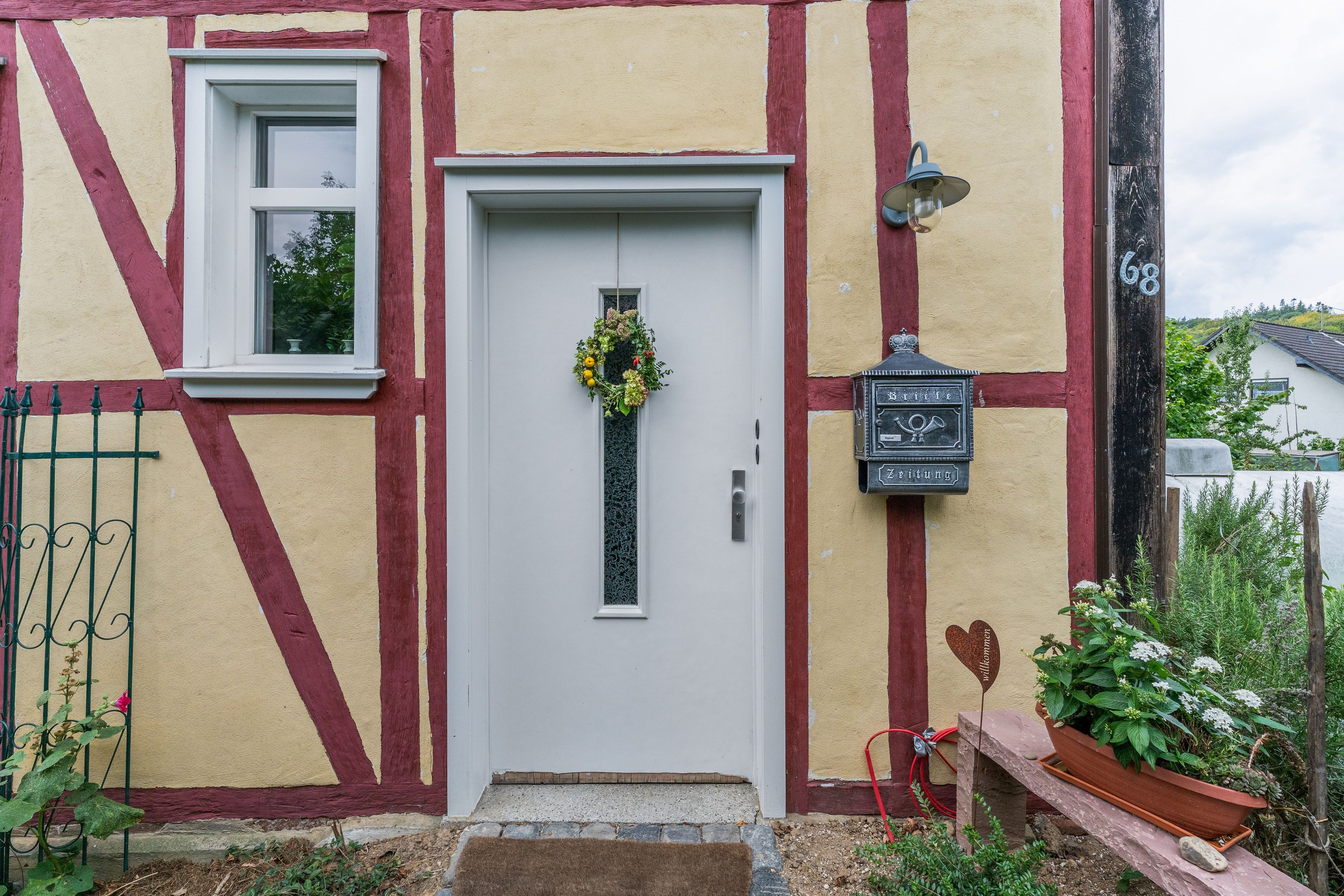 A traditional half-timbered house with a white door, a small window, and a welcome sign.