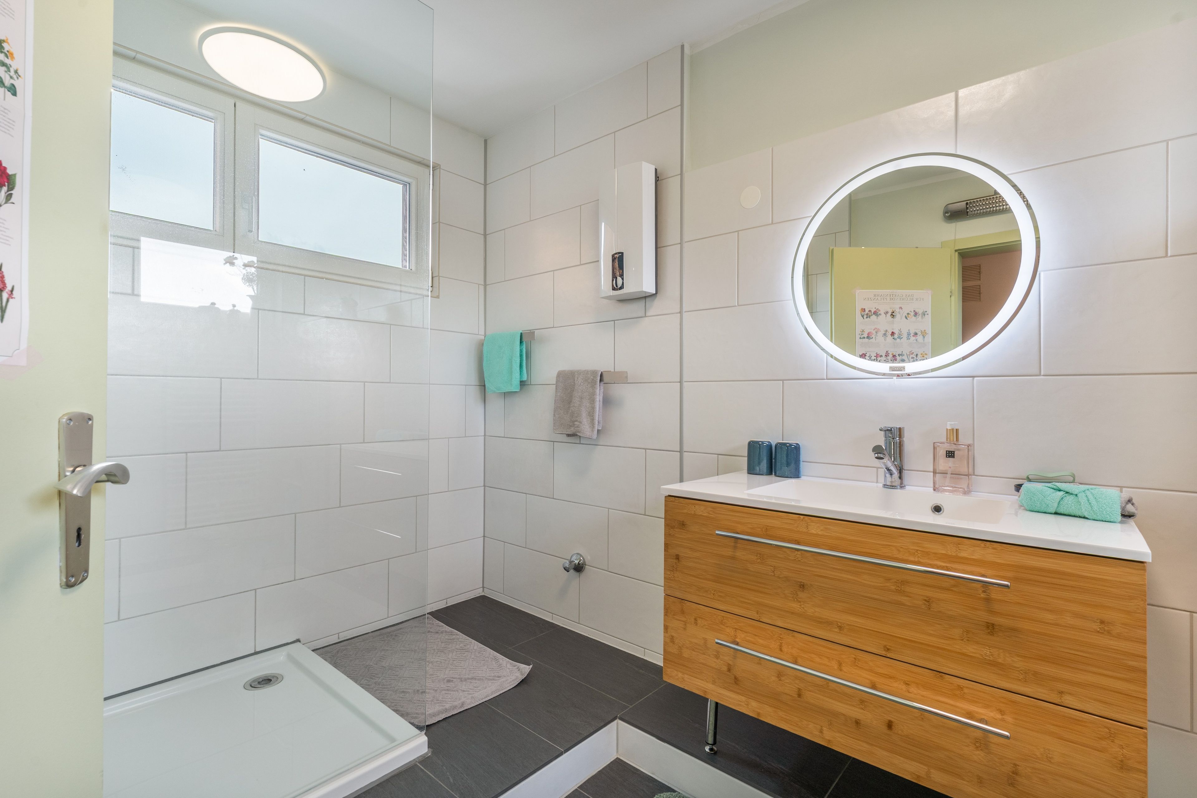 Ein modernes Badezimmer mit Dusche, Waschtisch inklusive Spiegel und einem Handtuchhalter.