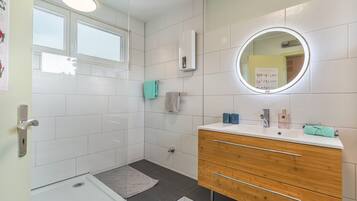 Ein modernes Badezimmer mit Dusche, Waschtisch inklusive Spiegel und einem Handtuchhalter.