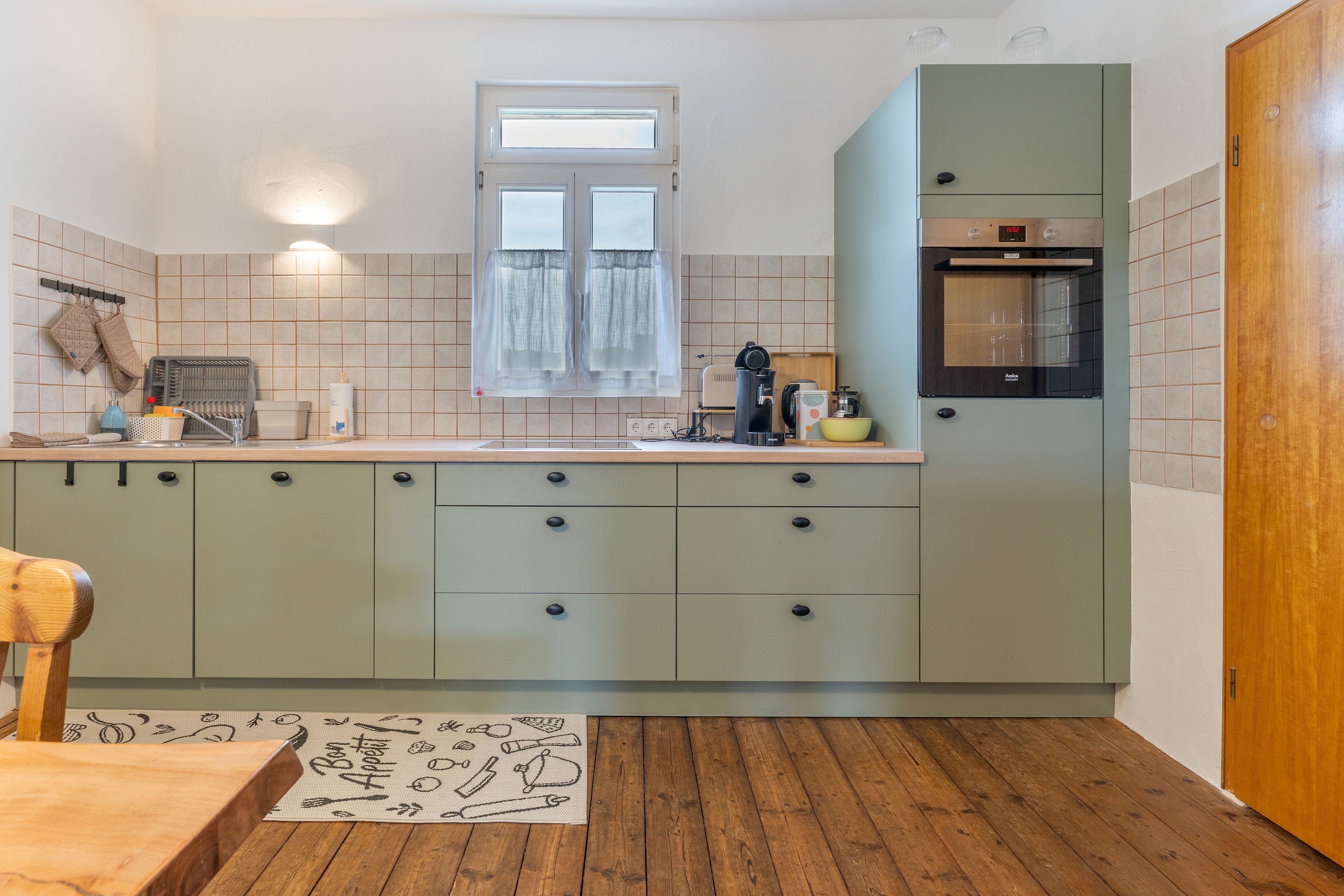 Una cocina compacta con ventana, horno empotrado y una mesa de comedor de madera.