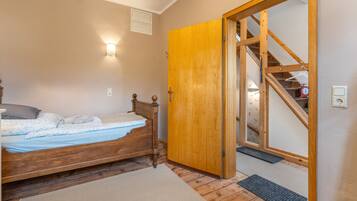 A bedroom with a wooden bed, a door leading to a staircase, and a wall-mounted light fixture.