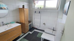 Ein modernes Badezimmer mit einem Holzkabinent, einem Waschbecken, einer Toilette und einem kleinen Tisch.