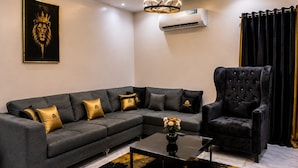 Una sala de estar moderna con un sofá seccional, un sillón capitoné, una mesa de centro de vidrio y una alfombra decorativa negra y dorada.