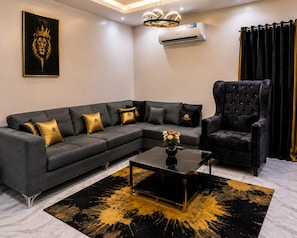 A modern living room with a sectional sofa, a tufted armchair, a glass coffee table, and a black and gold accent rug.