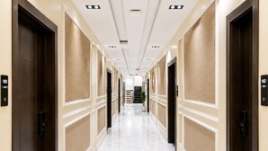 Un pasillo de hotel con suelo de mármol, paredes color beige y puertas de madera oscura.