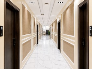 A hotel corridor with marble flooring, beige walls, and dark wood doors.