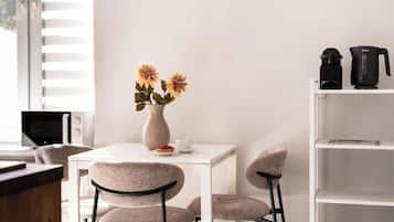 A modern room with a white table, two chairs, a vase with flowers, a coffee maker, and a TV.