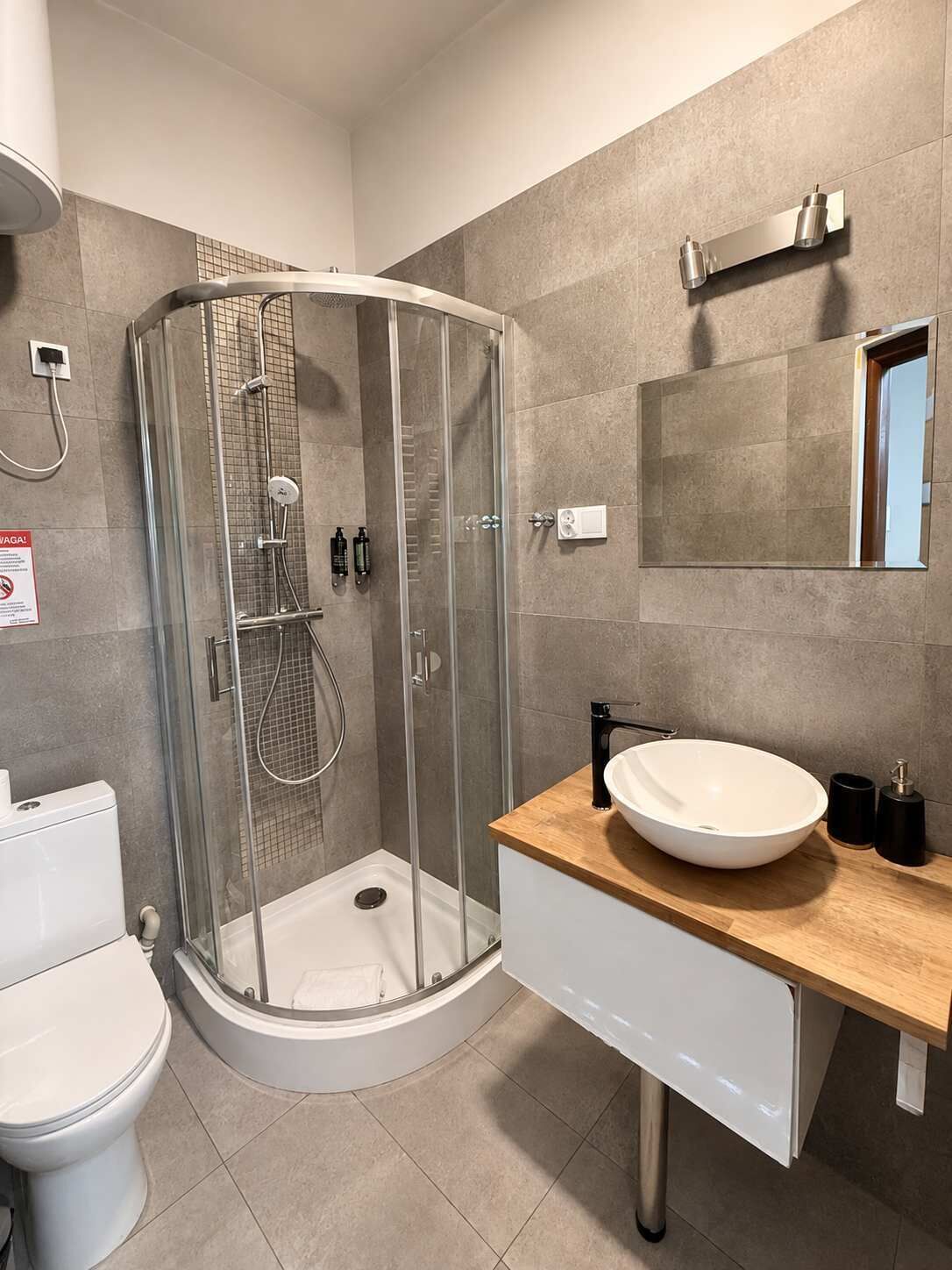 Un bagno moderno con doccia vetro, lavandino bianco e specchio sopra il piano di lavoro.