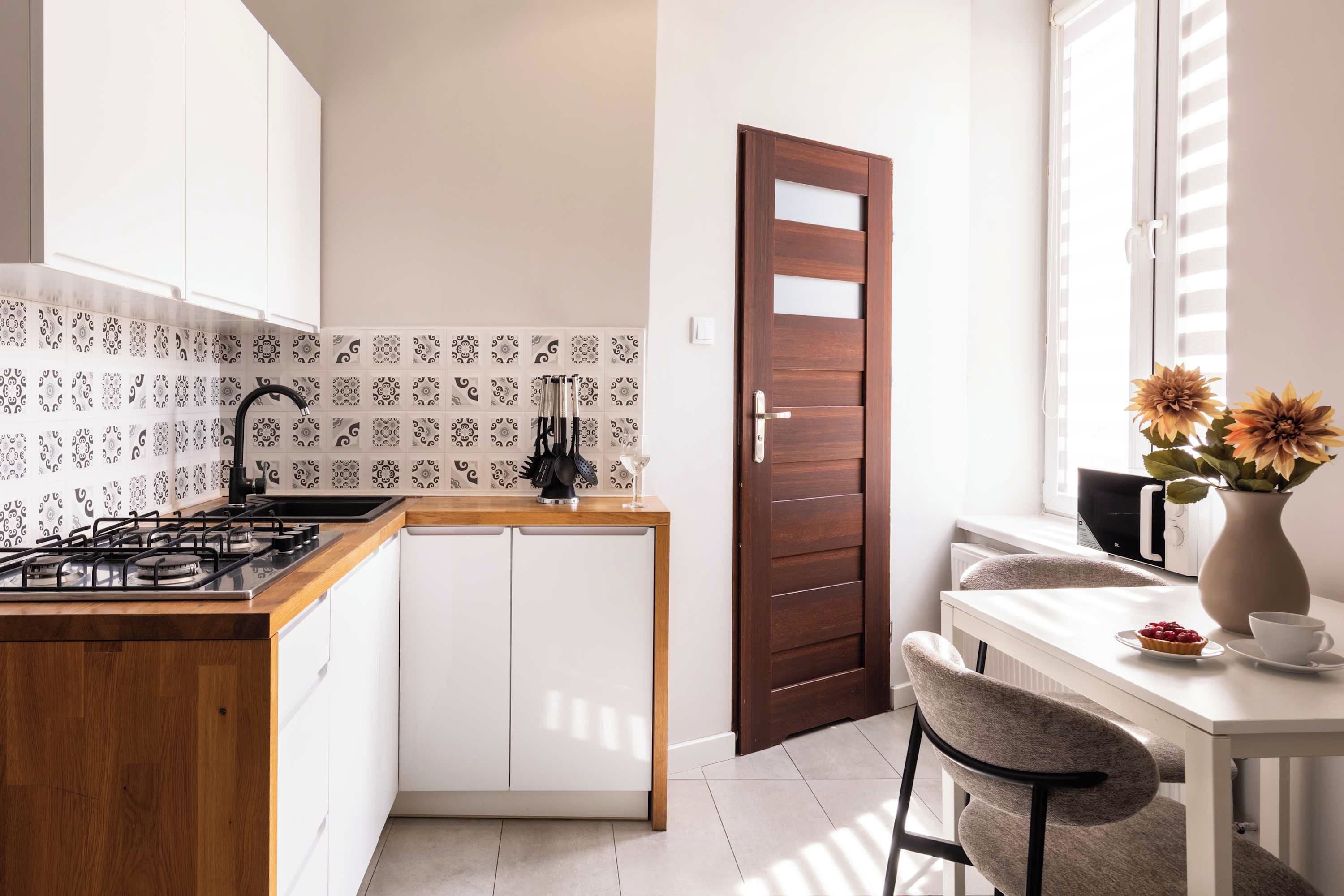 Una cocina moderna con estufa a gas, armarios blancos, salpicadero con diseño y puerta de madera.