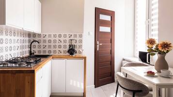 Una cocina moderna con estufa a gas, armarios blancos, salpicadero con diseño y puerta de madera.
