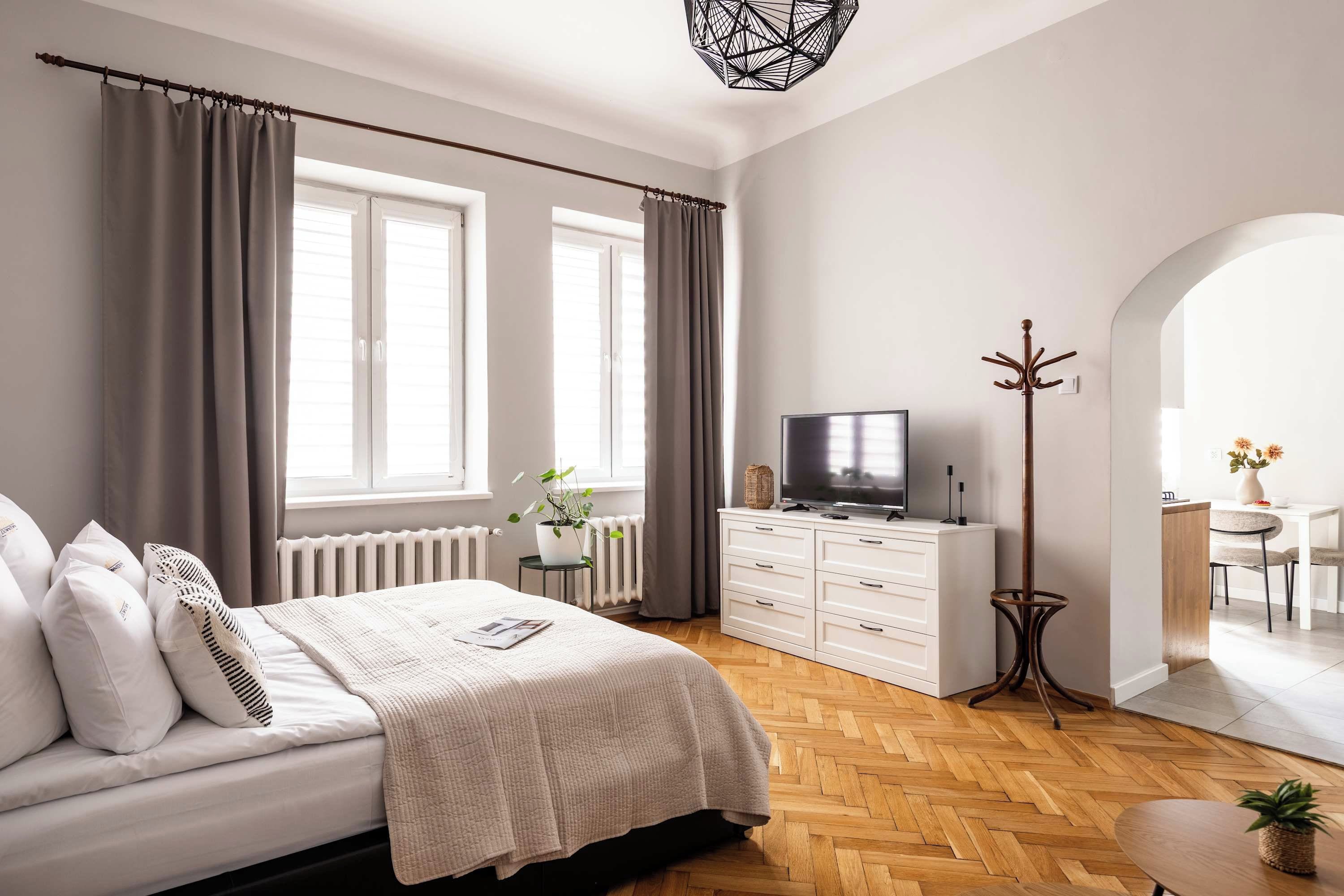 A modern bedroom with a bed, a TV, a coat rack, and a dining area.