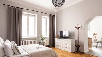 A modern bedroom with a bed, a TV, a coat rack, and a dining area.