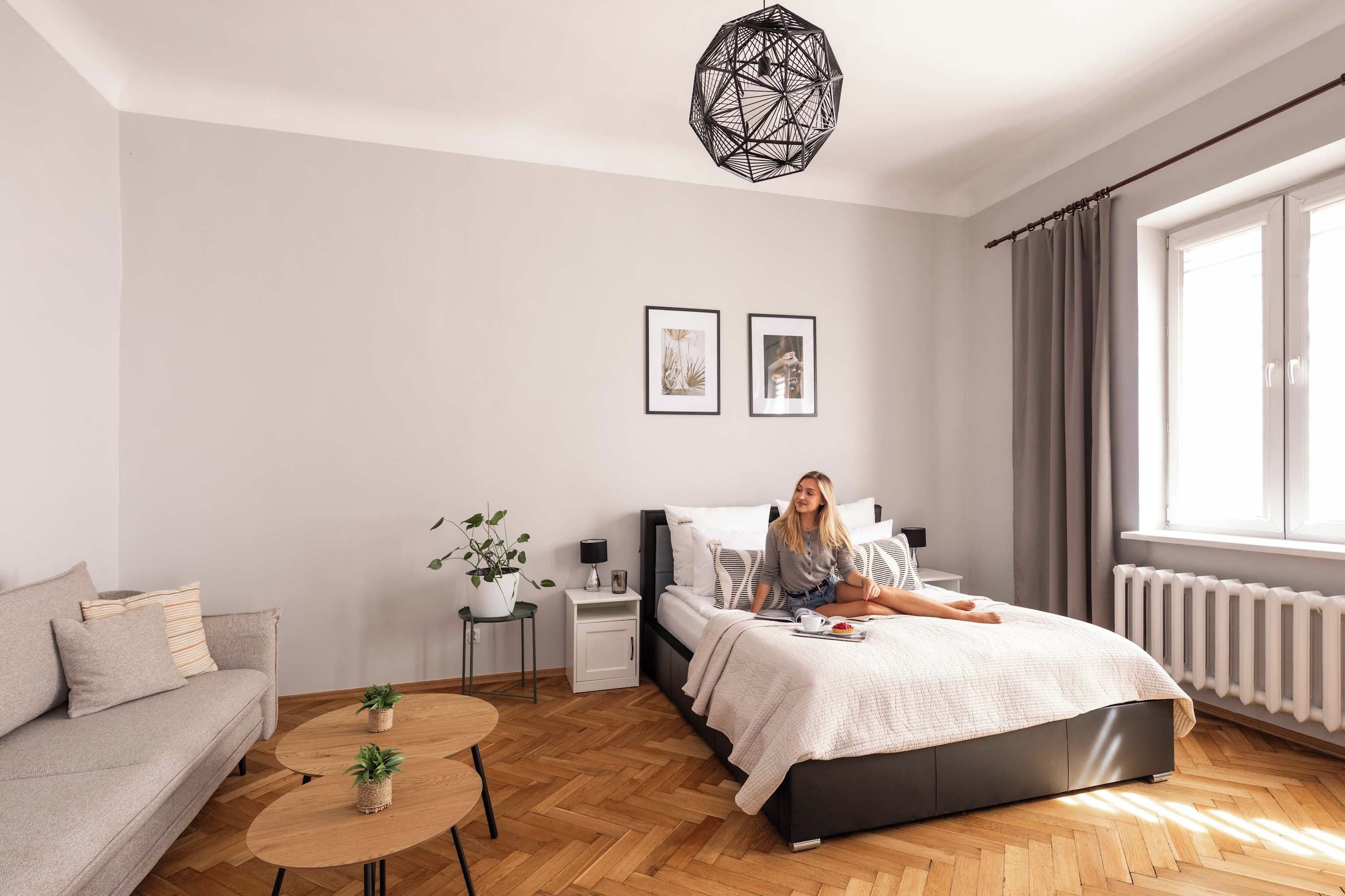 A modern bedroom with a bed, a sofa, a small table, and a potted plant.