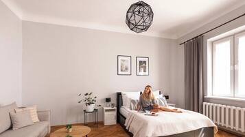 A modern bedroom with a bed, a sofa, a small table, and a potted plant.